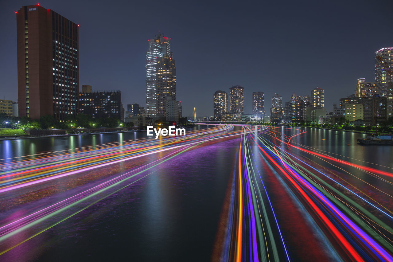 Light trails on illuminated buildings against sky at night