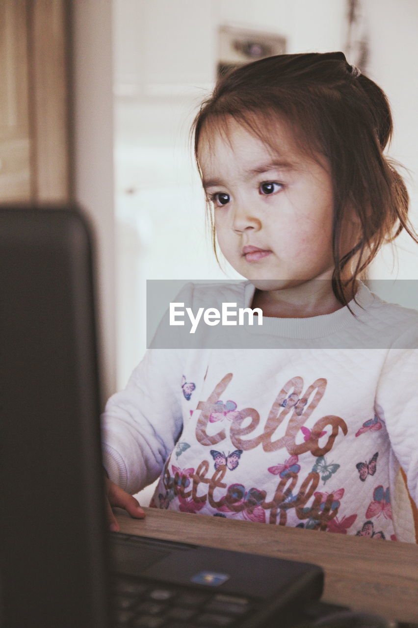 Cute girl looking away while using laptop on table