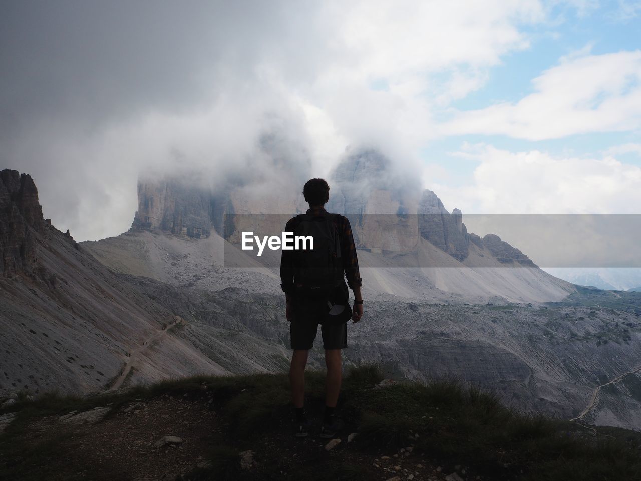 REAR VIEW OF MAN STANDING ON LANDSCAPE AGAINST SKY