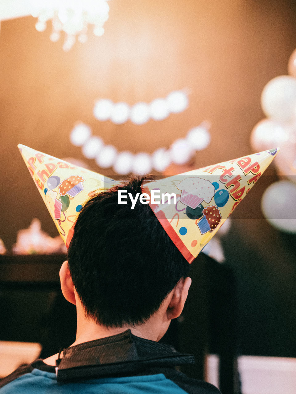 Rear view of a boy wearing 2 birthday cones on his head
