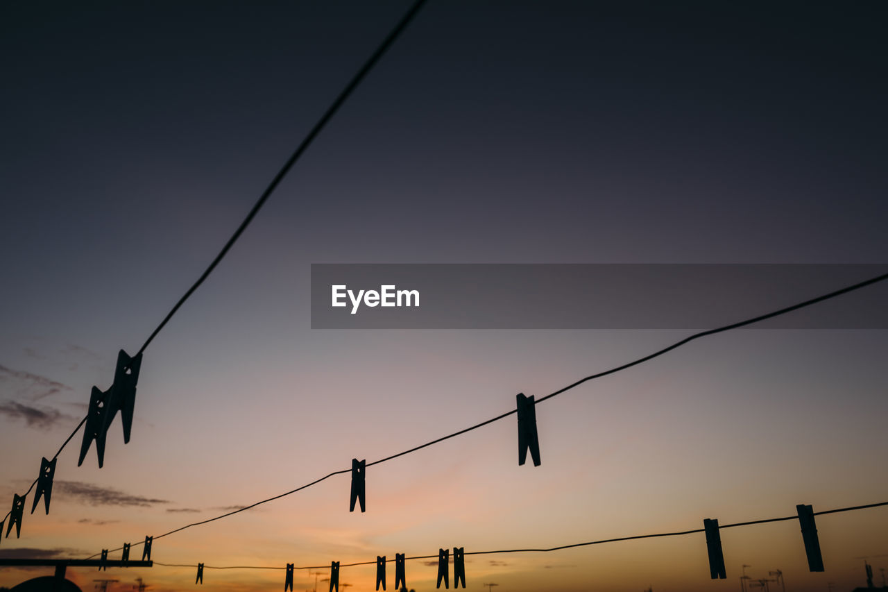 Silhouette clothespins hanging on clotheslines against sky during sunset