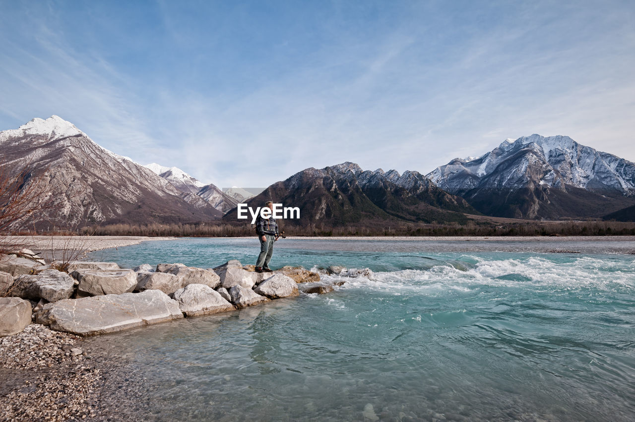 Man standing on rocks by lake against mountains