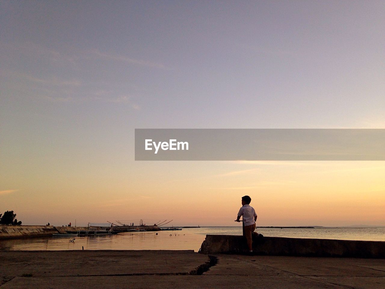 Rear view of boy standing on pier against sky during sunset