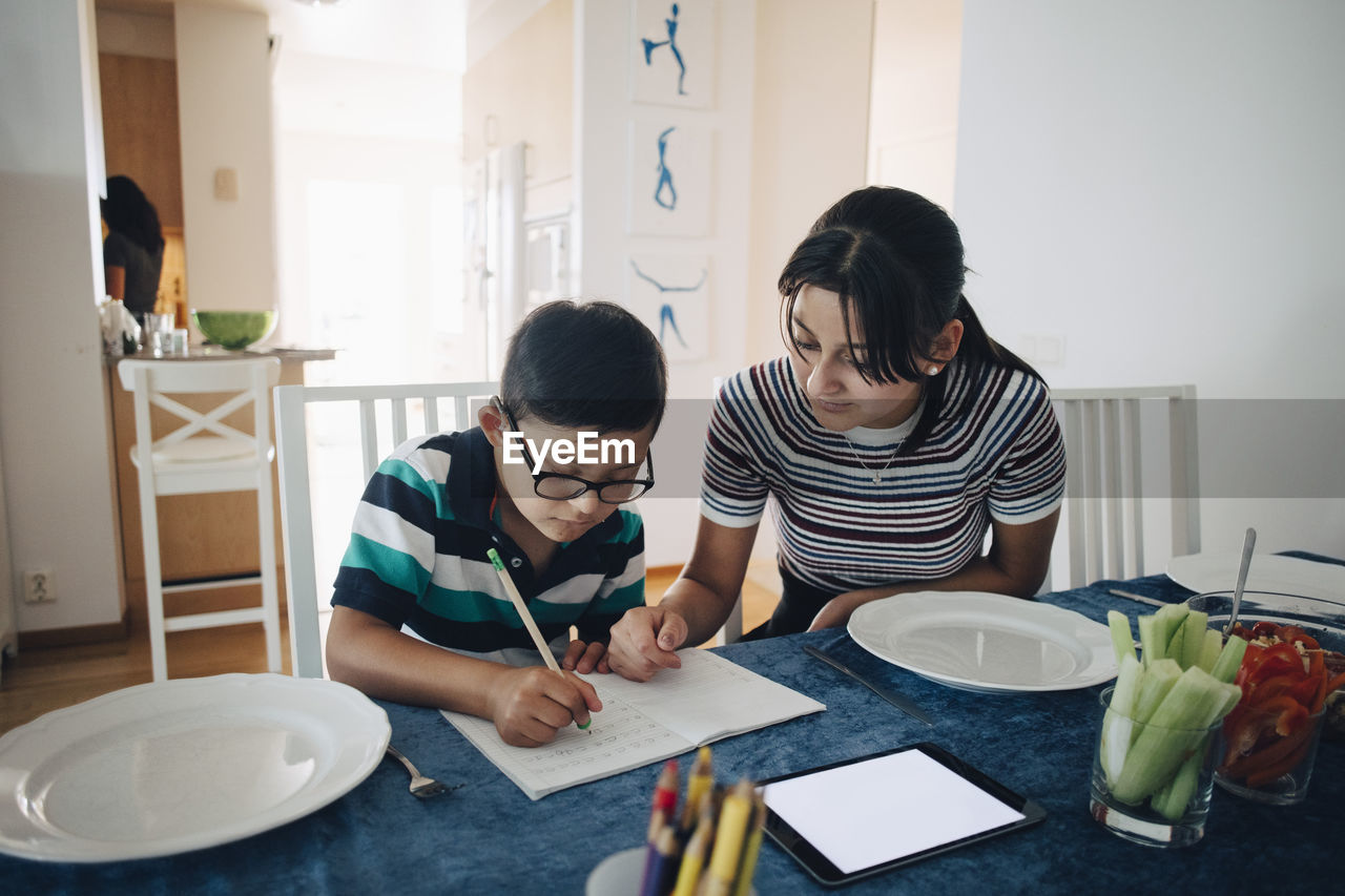 Teenage girl assisting brother in homework at dining table