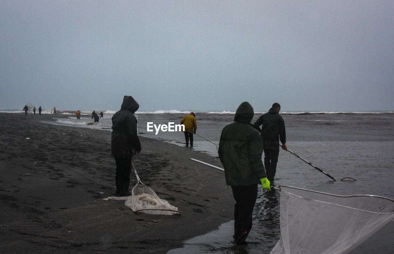 REAR VIEW OF PEOPLE WALKING ON BEACH