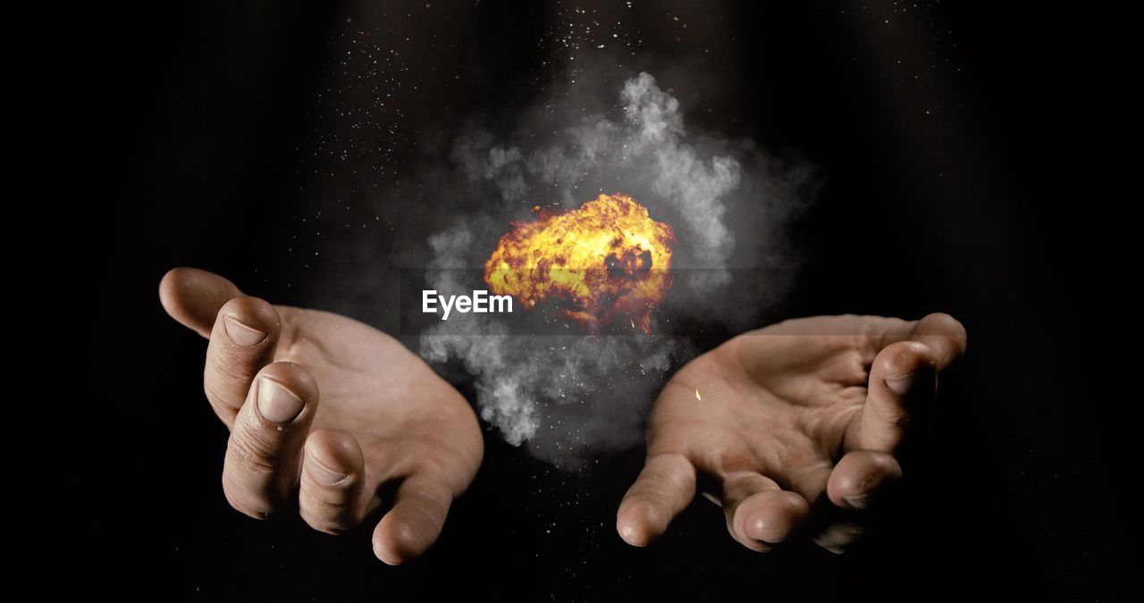 Digital composite image of hands with fire against black background
