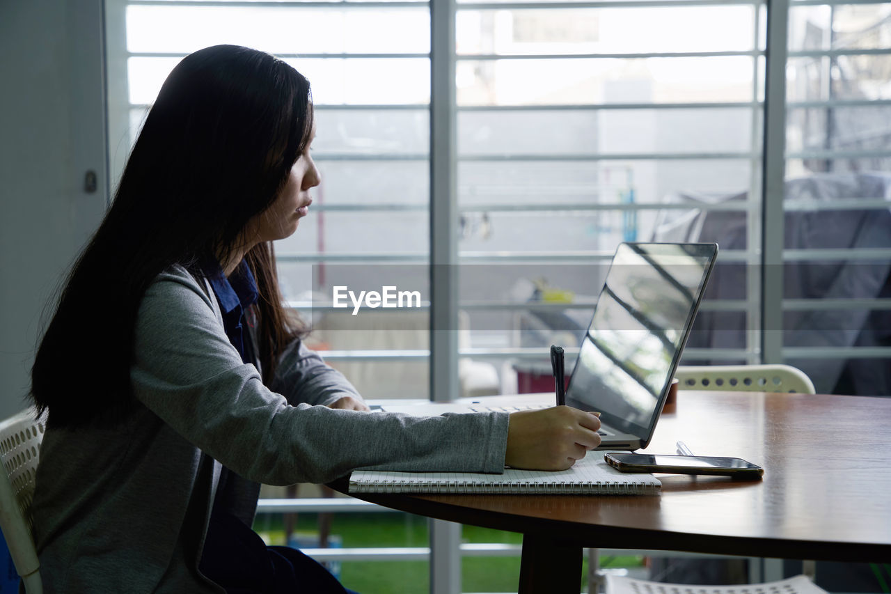 SIDE VIEW OF A WOMAN WORKING ON TABLE IN OFFICE