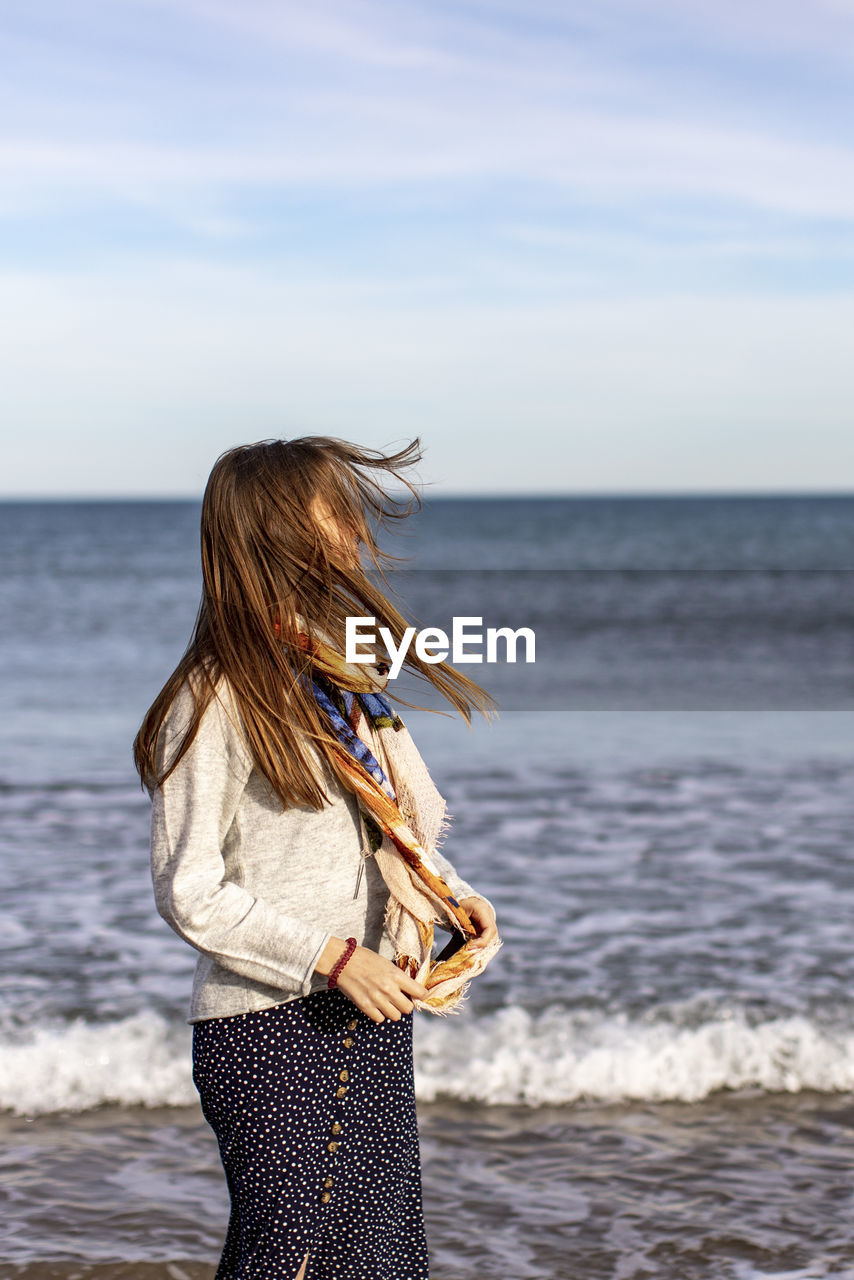 Rear view of woman standing at beach against sky