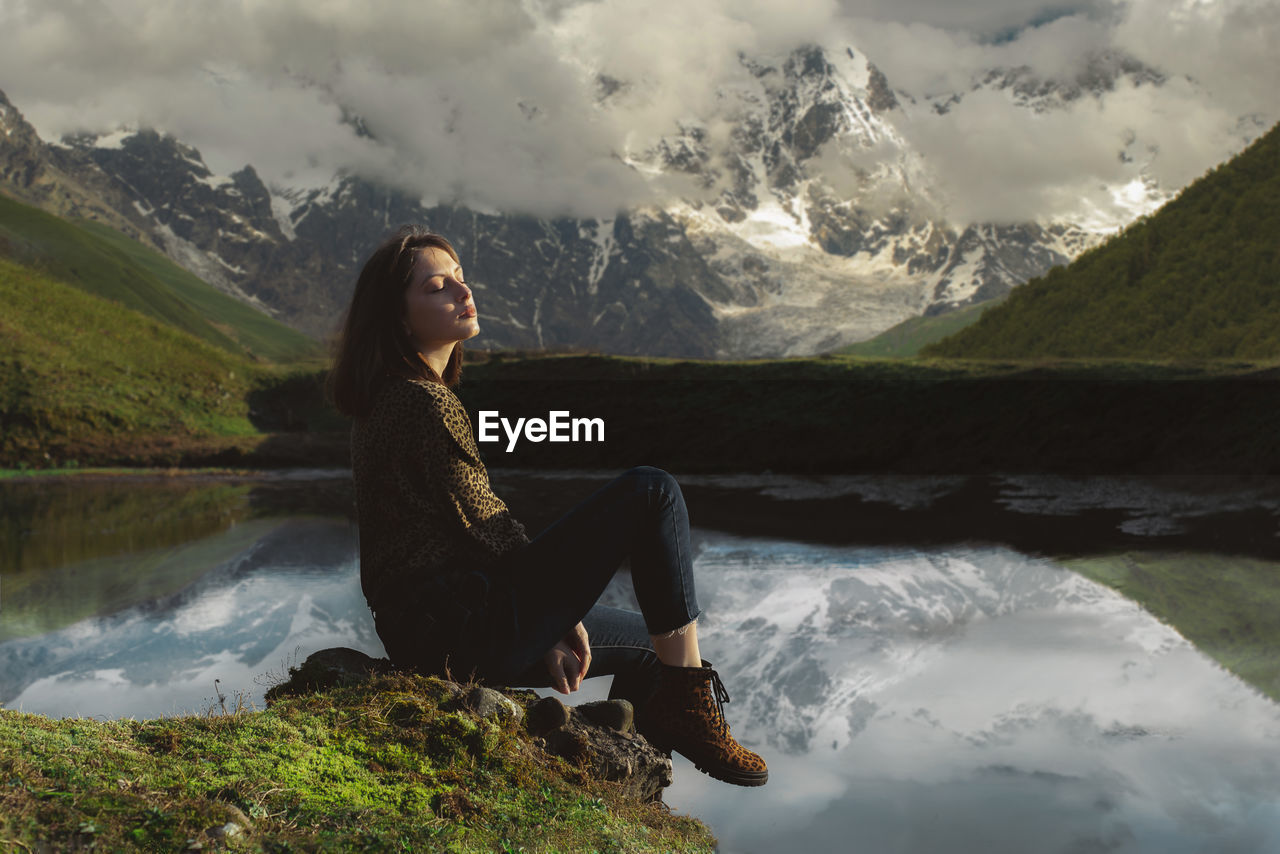 Georgian girl sits near the lake and around is beautiful nature