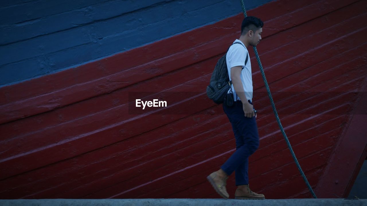 Side view of young man with backpack walking on retaining wall