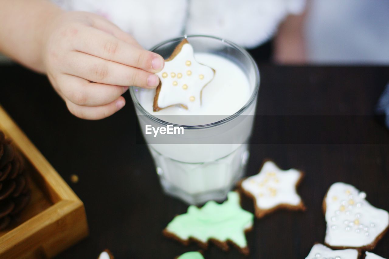 Cropped image of child dunking star shape cookie in milk