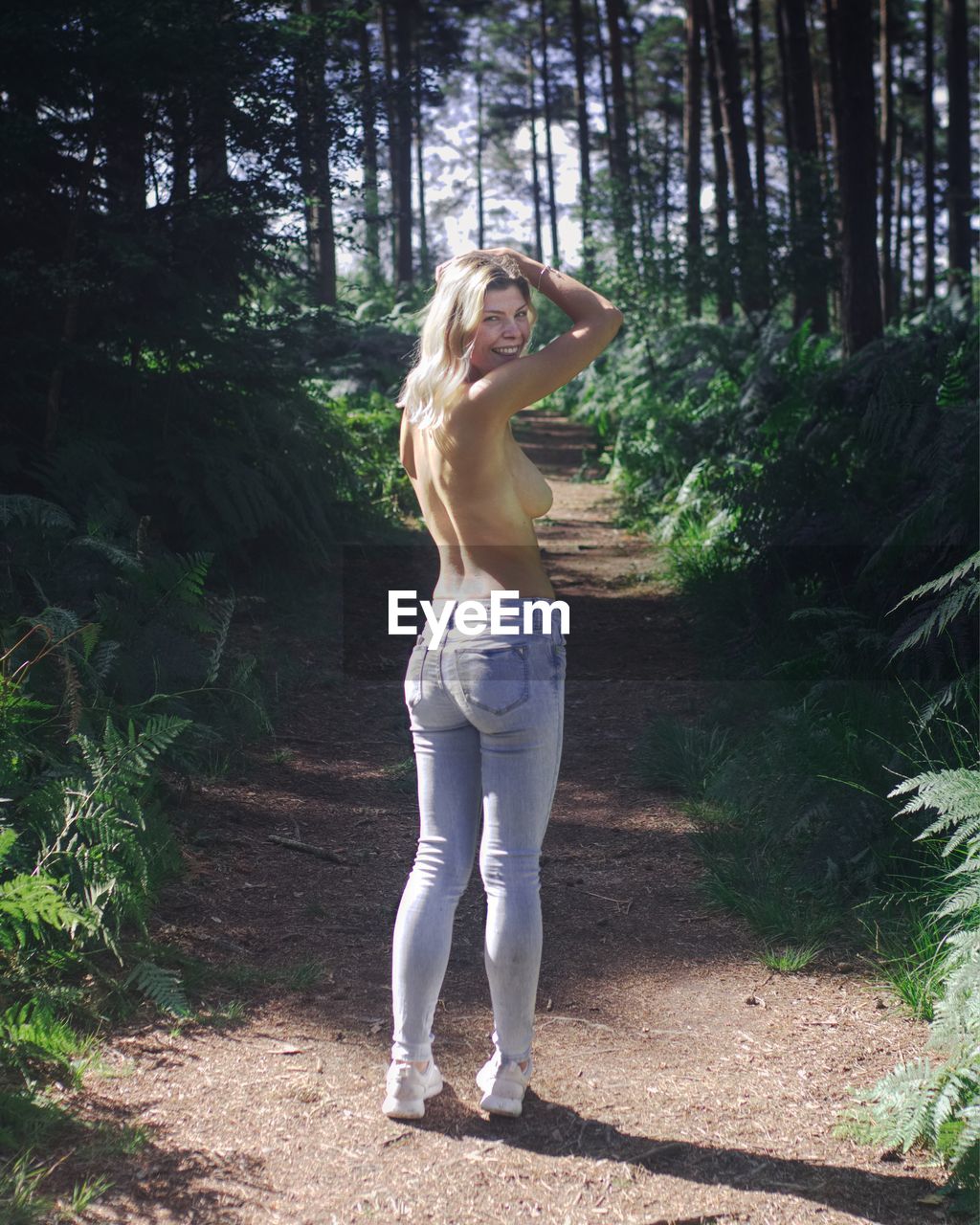 Portrait of shirtless young woman standing on field in forest