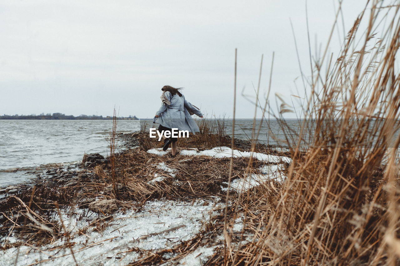 Man walking on snow covered land against sky