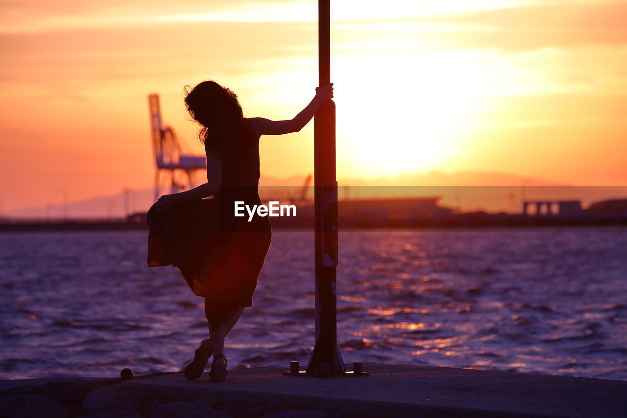 Silhouette woman standing on pier over sea against sky during sunset