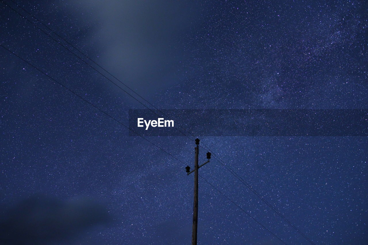 Low angle view of electricity pylon against star field at night