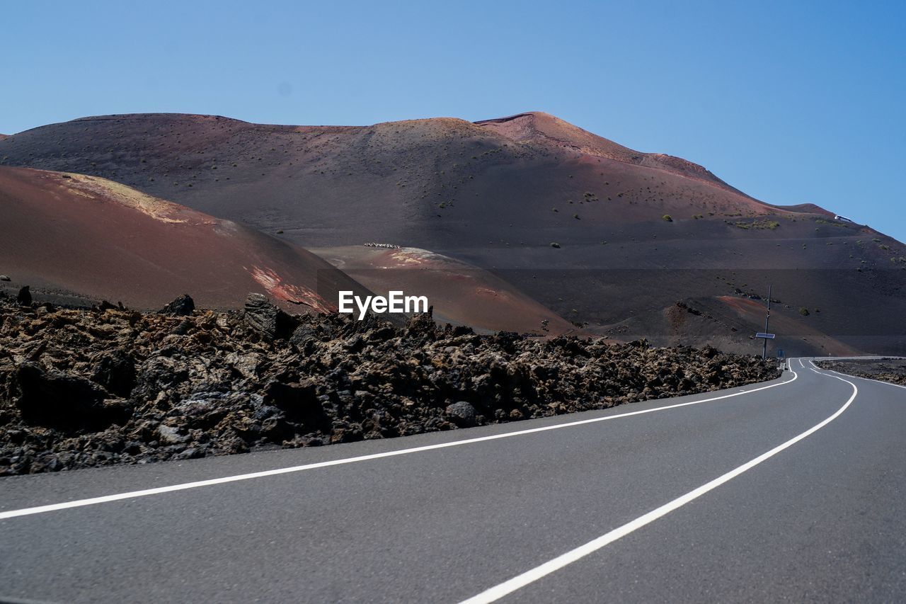 Scenic view of road by mountains against clear sky