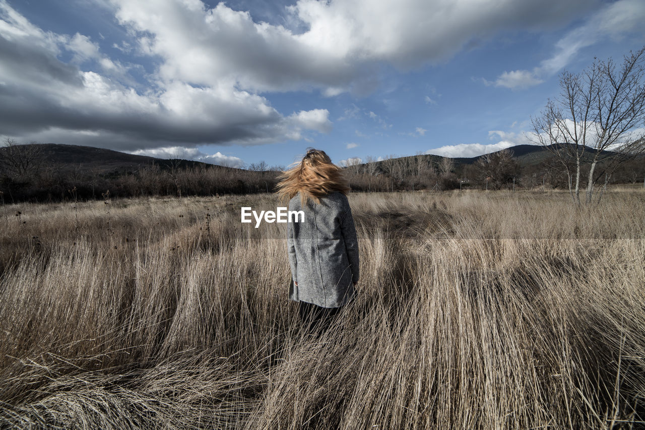 Rear view of woman standing on field against sky