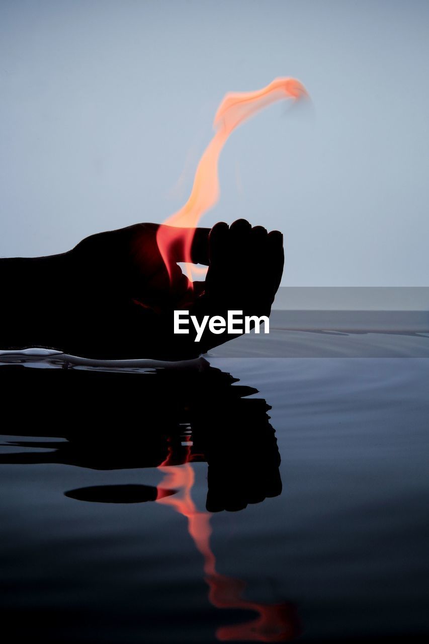 Cropped hand holding fire over water with reflection