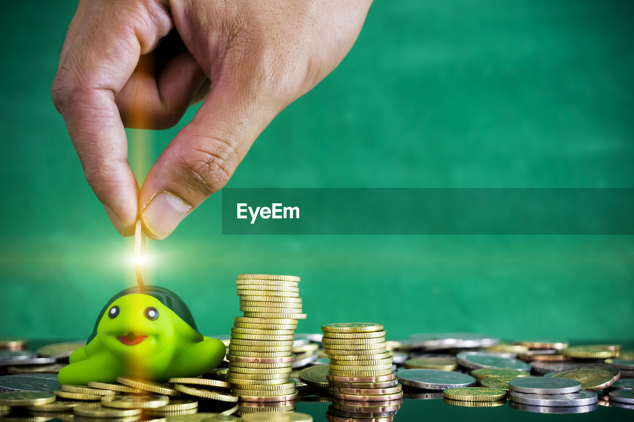 Cropped hand of person putting coin in piggy bank on table