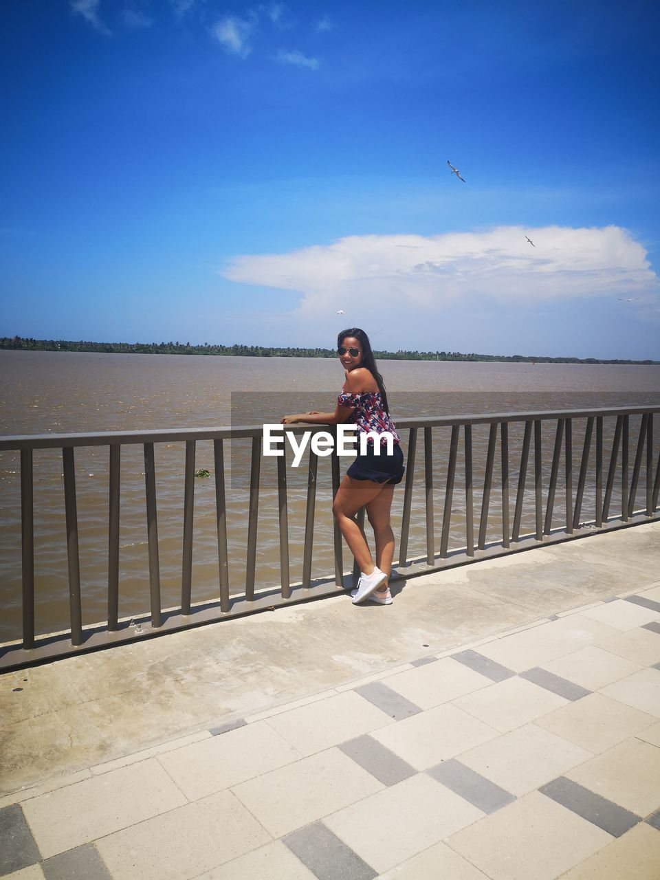 WOMAN STANDING ON RAILING AGAINST SEA