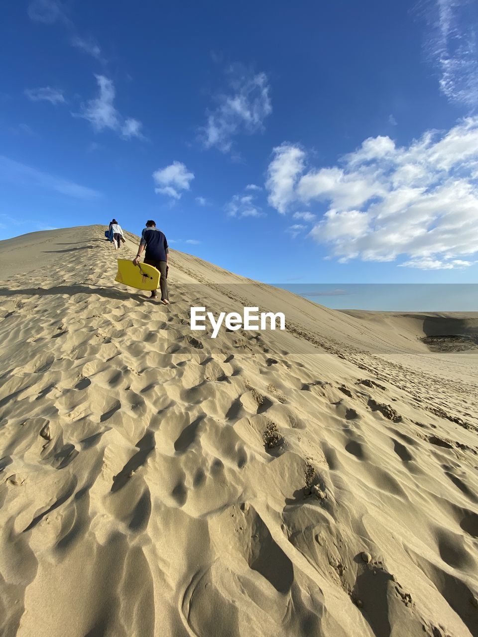 Low angle view of man walking up a sand dune with a body board