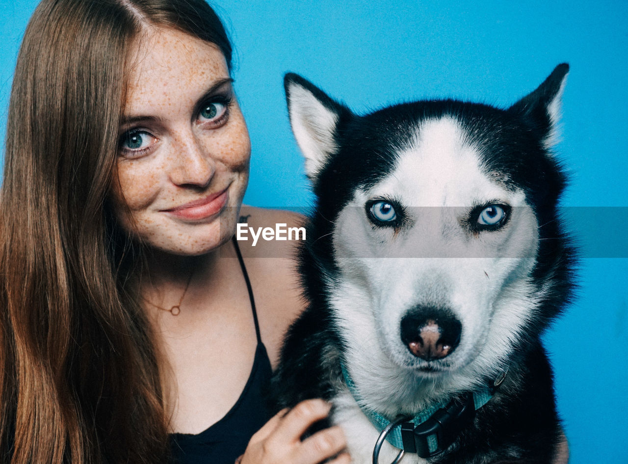 Close-up portrait of woman with siberian husky against blue background