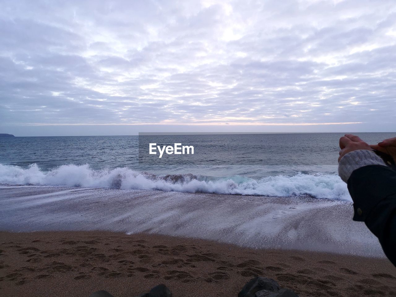 Cropped hands of person against sea during sunset