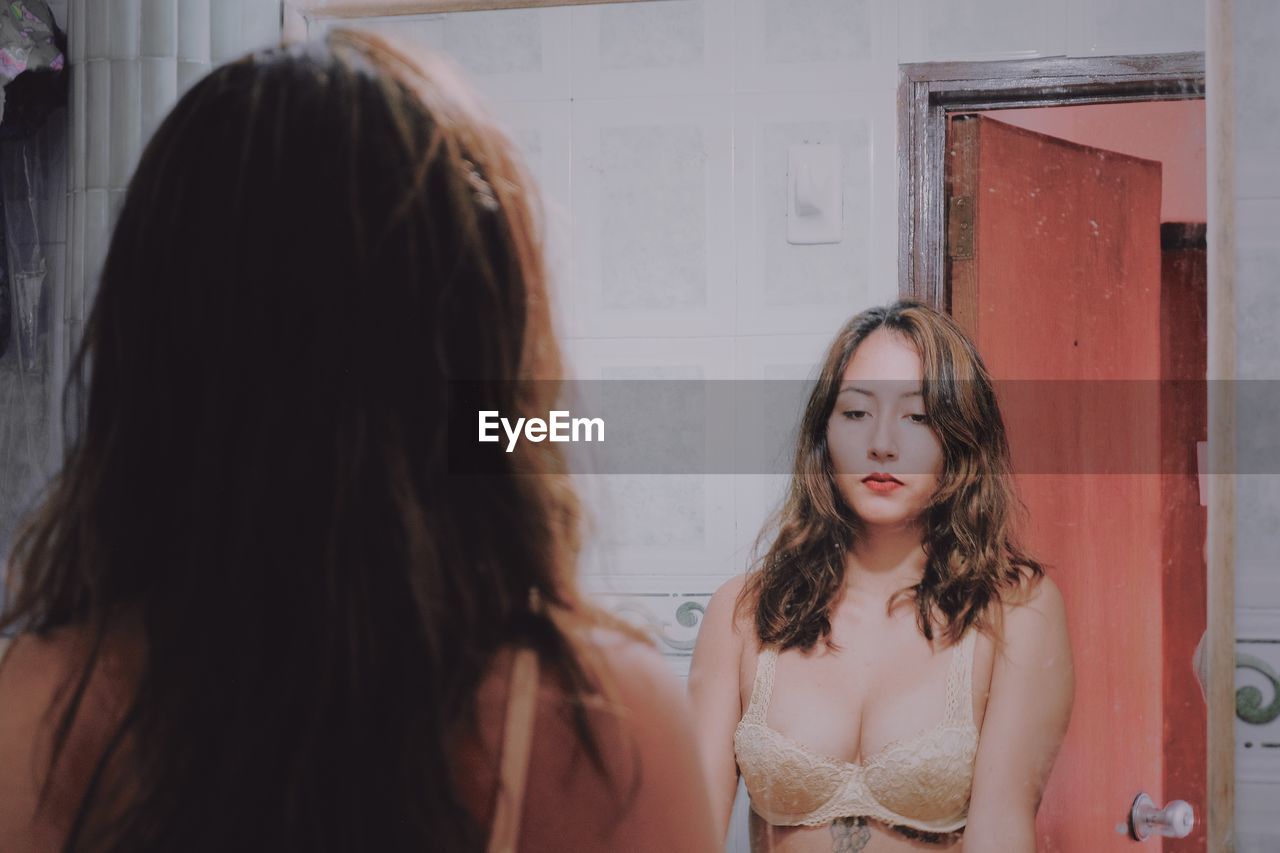 Young woman in bra standing against mirror