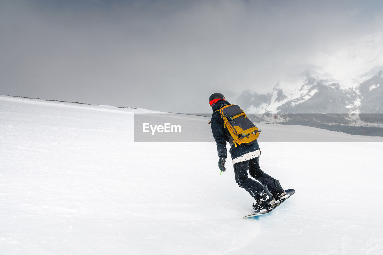Freeride snowboarder rolls down a snowy slope, leaving behind a trail on the background of mountains
