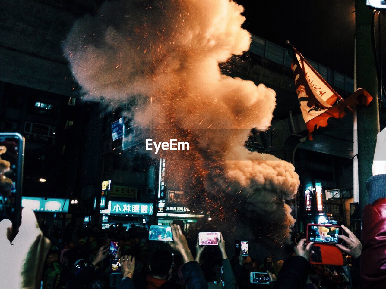 People photographing firework smoke during festival in city at night