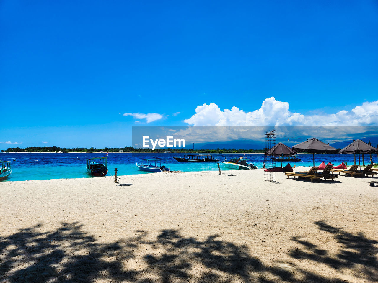 land, beach, sky, sea, water, sand, ocean, nature, body of water, blue, scenics - nature, holiday, travel destinations, vacation, trip, beauty in nature, shore, sunlight, travel, coast, tranquility, sunny, tranquil scene, horizon, summer, tourism, cloud, day, bay, outdoors, idyllic, clear sky, coastline, relaxation, no people, tropical climate, shadow, environment, horizon over water, landscape, chair, wave, island, nautical vessel, hut