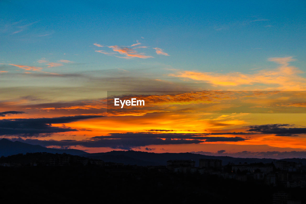 Scenic view of dramatic sky over silhouette landscape during sunset