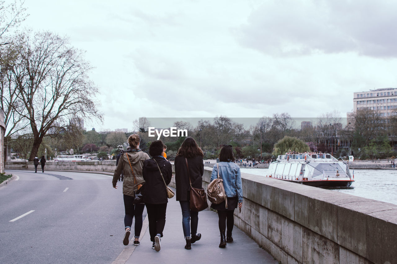 Rear view of people walking on road by river against sky