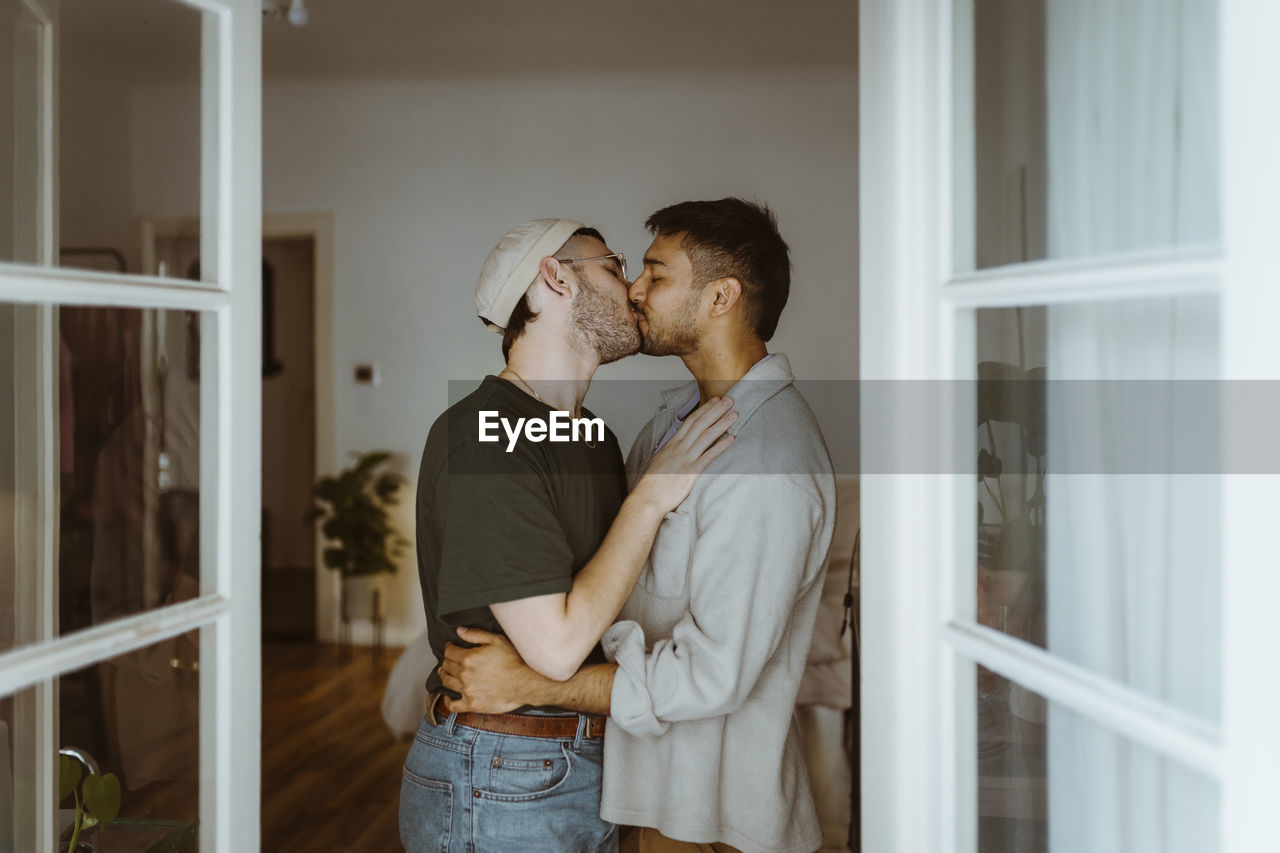Side view of romantic gay couple kissing each other seen through doorway