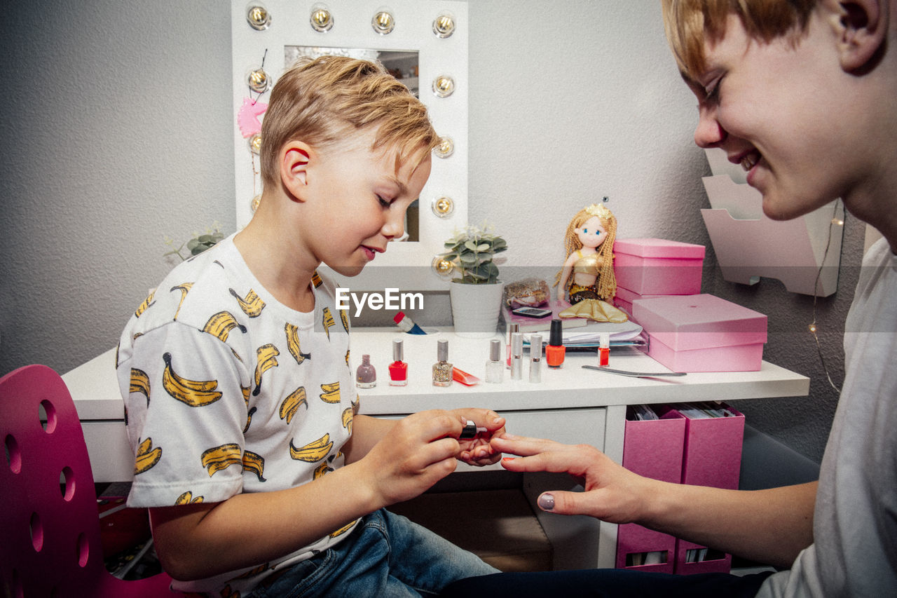 Boy applying nail polish on brother in bedroom
