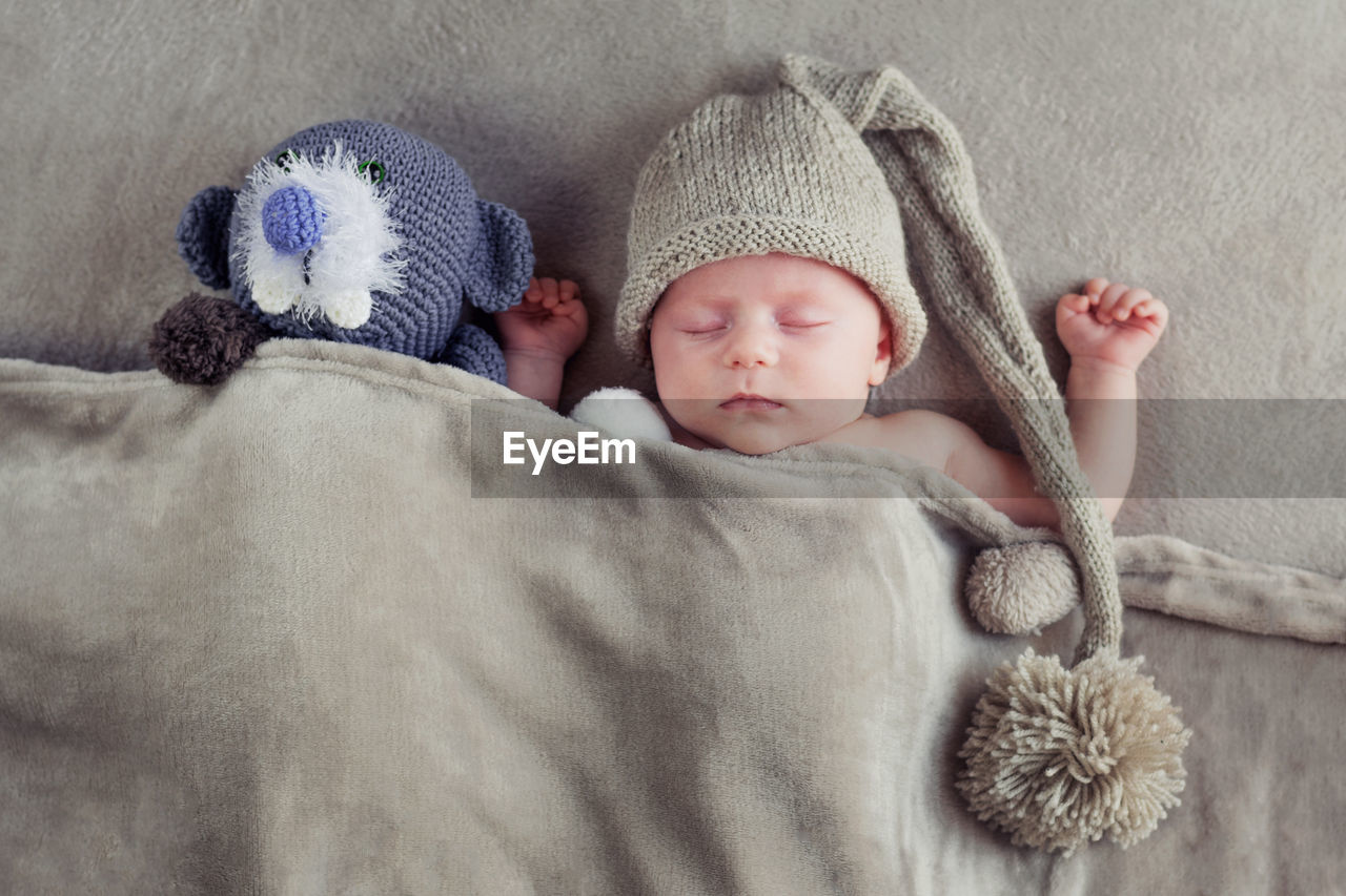 Directly above shot of cute baby boy with stuffed toy sleeping on bed