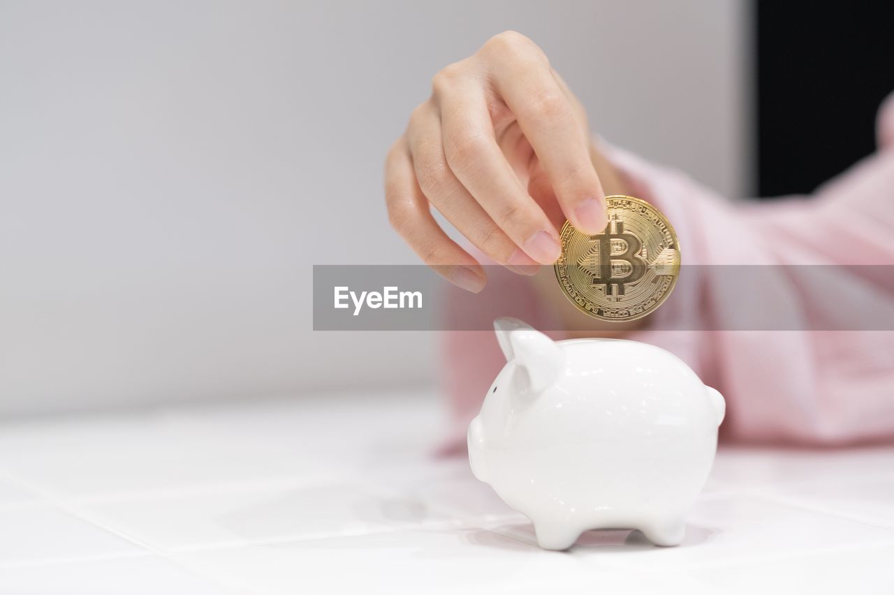 Close-up of woman hand inserting coin in piggy bank on table