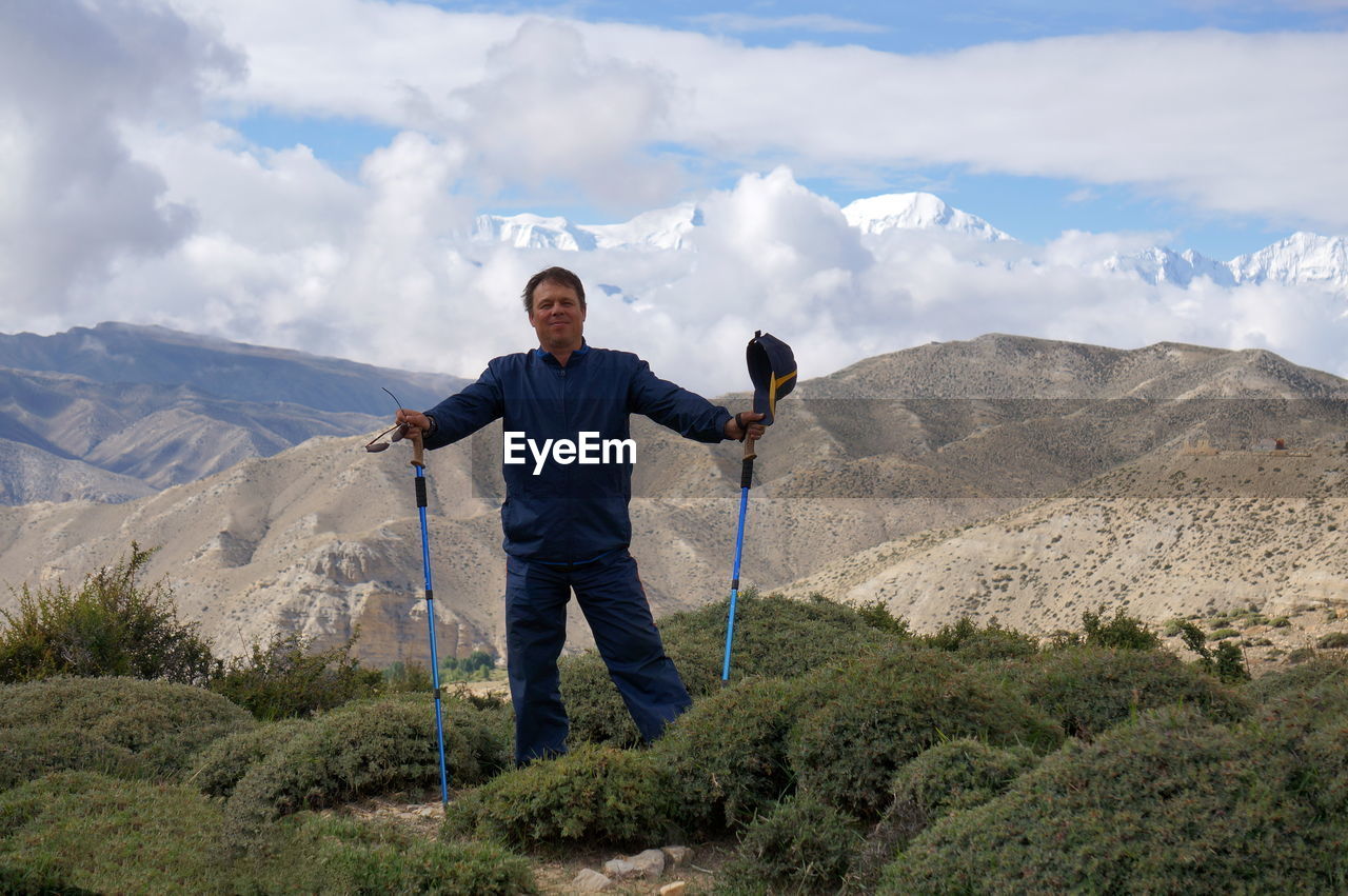 Smiling tourist stands with trekking sticks, against the backdrop of the annapurna massif.