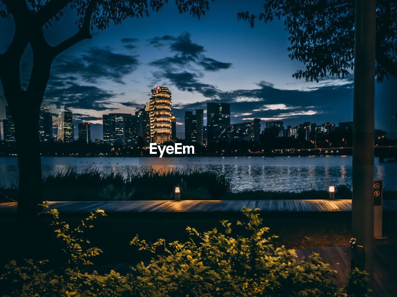 ILLUMINATED BUILDINGS BY RIVER AGAINST SKY IN CITY