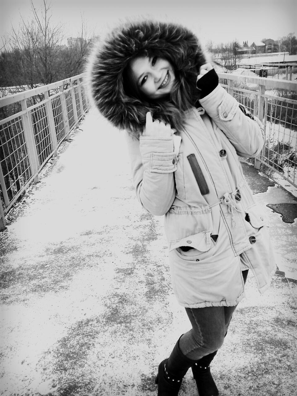 Portrait of happy woman wearing fake fur jacket while standing on elevated walkway during winter
