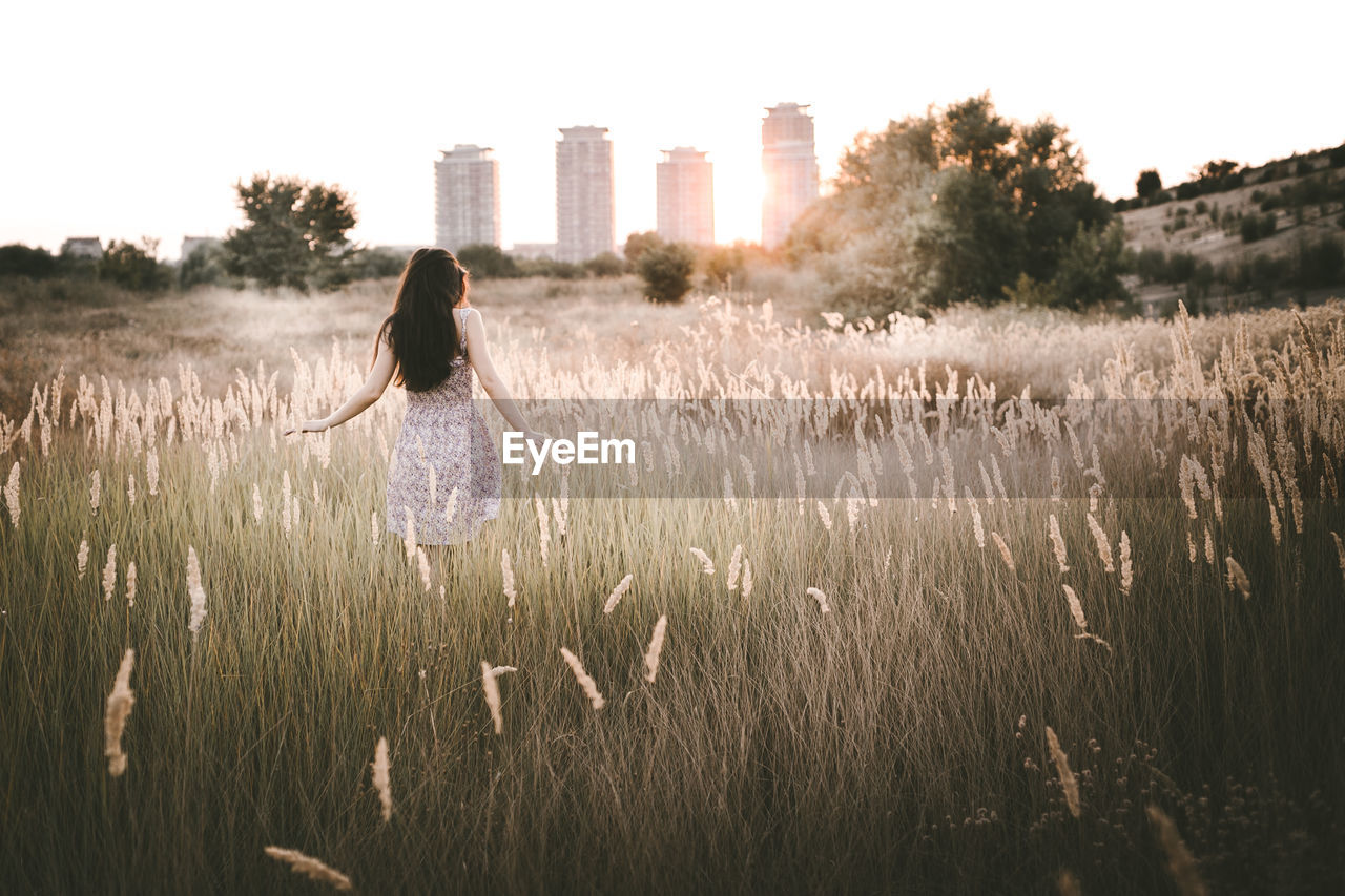 Rear view of young woman walking on grassy field during sunset