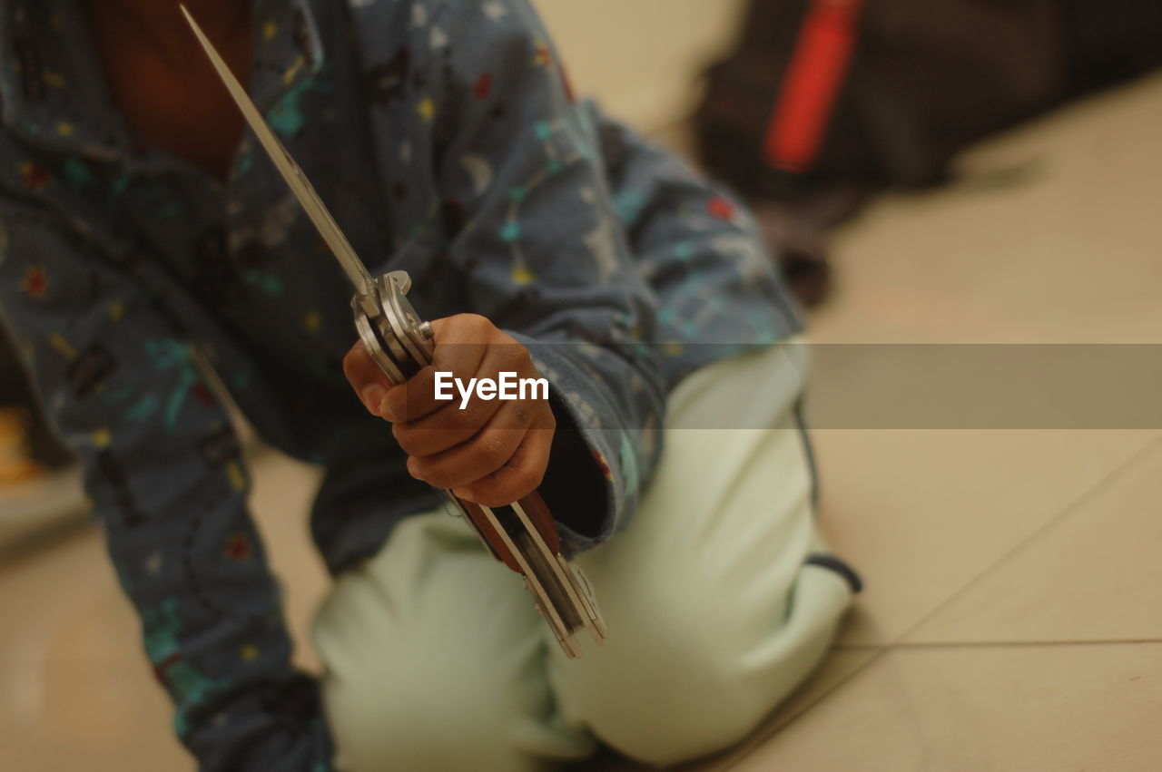 Close-up of boy holding knife while kneeling on floor