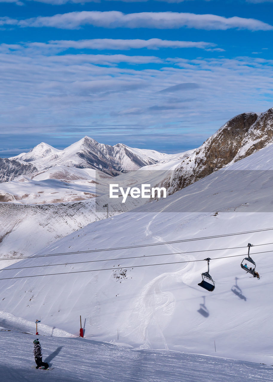 Overhead cable cars by snow covered mountains against cloudy sky