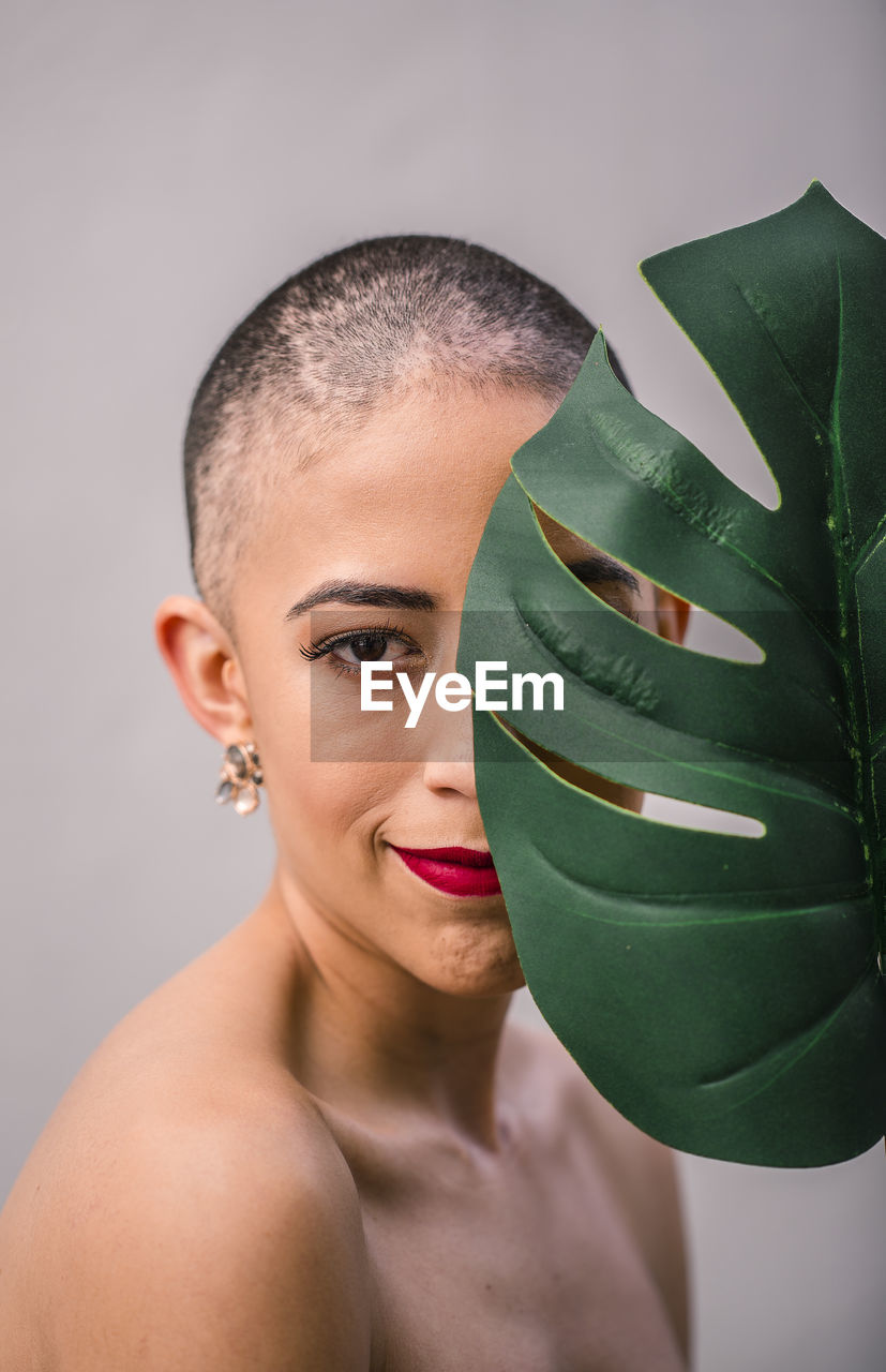 Portrait of young woman holding monstera leaf