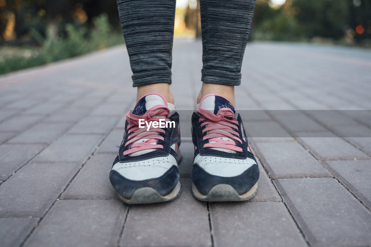 LOW SECTION OF WOMAN WEARING SHOES STANDING ON FOOTPATH