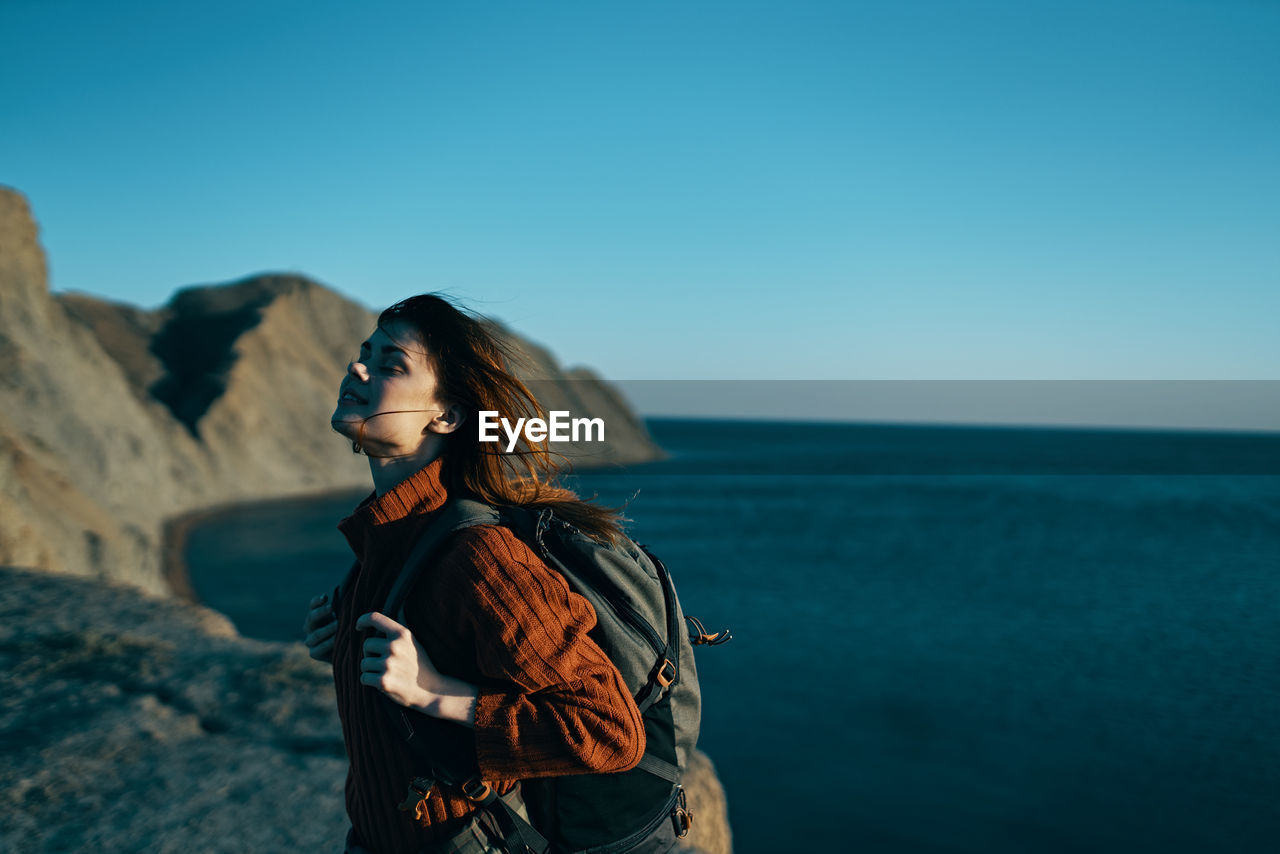 WOMAN STANDING AT SEA AGAINST SKY