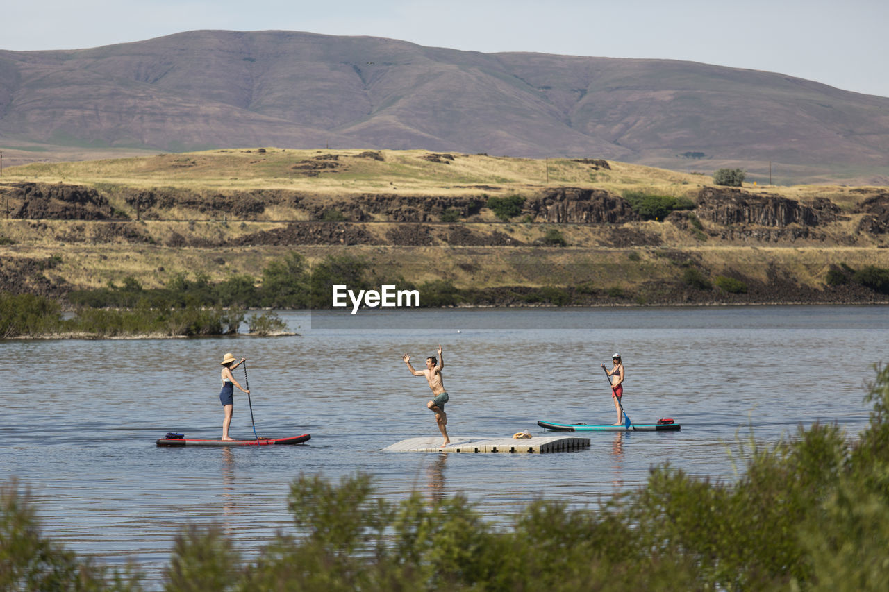 Two friends watch a young man jump off a dock in the columbia river.