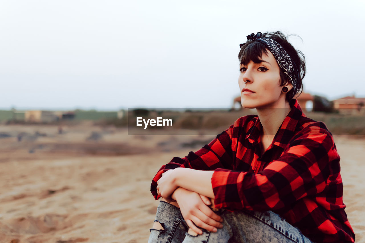 Thoughtful hipster woman sitting on sandy beach