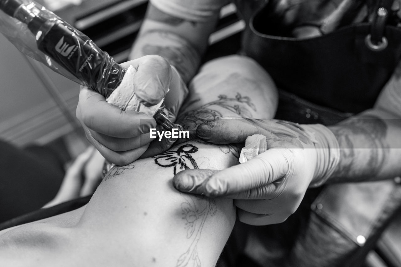 Cropped image of artist making tattoo on hand of customer