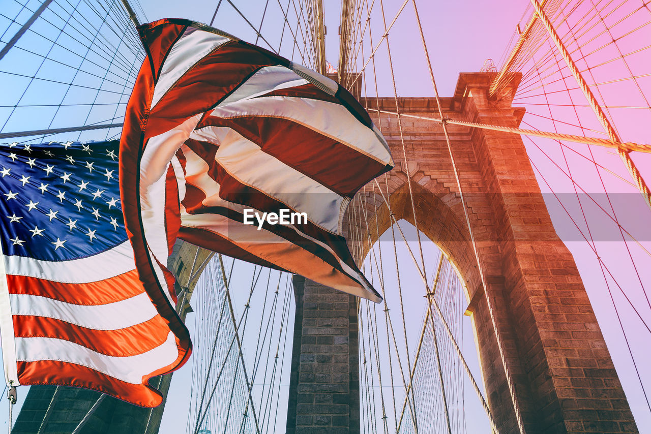 Low angle view of american flag against brooklyn bridge during sunset